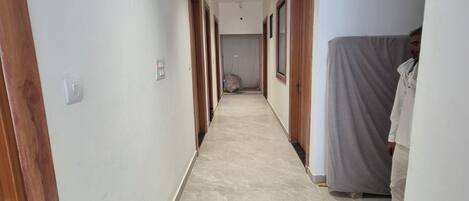 Un pasillo con puertas de madera, piso de baldosas y una persona al fondo.