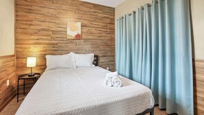 A neatly made bed with white bedding, a wooden headboard, a nightstand with a lamp, and light blue curtains. - Quiet Ranch Retreat for Work Crews & Families Johnstown, OH (Johnstown)