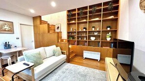 A modern living room with a sofa, a small table, a bookshelf, and a radiator. - MetaWiseBnB Stylish Loft Studio with Garden in Seaforth (Seaforth)