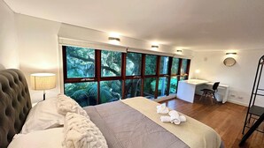 A bedroom with a large bed, a desk, and a view of a forest through large windows. - MetaWiseBnB Stylish Loft Studio with Garden in Seaforth (Seaforth)