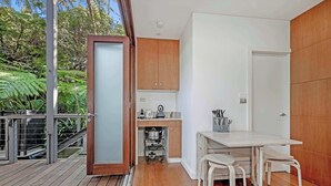 A modern kitchen with wooden cabinets, a white countertop, and a dining area with a table and chairs. - MetaWiseBnB Stylish Loft Studio with Garden in Seaforth (Seaforth)