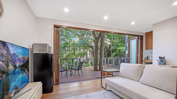 A modern living room with a large flat-screen TV, a black refrigerator, a beige sofa, and a dining area with a table and chairs. - MetaWiseBnB Stylish Loft Studio with Garden in Seaforth (Seaforth)