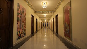 Un long couloir bien éclairé, orné de décorations élaborées au plafond et de tableaux encadrés accrochés aux murs.