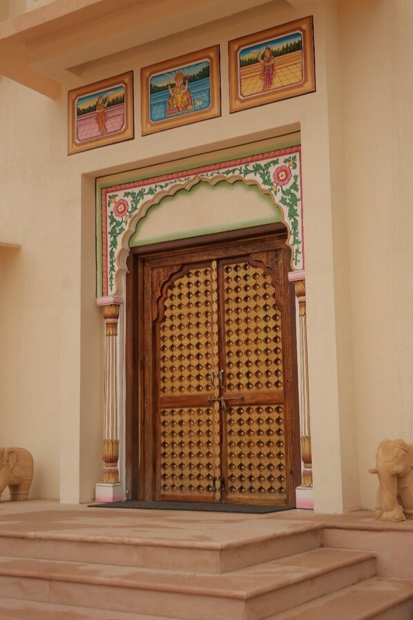 A traditional wooden door with intricate carvings, flanked by decorative pillars and framed artwork above. - Agastya Vilas Resort (Sujangarh)