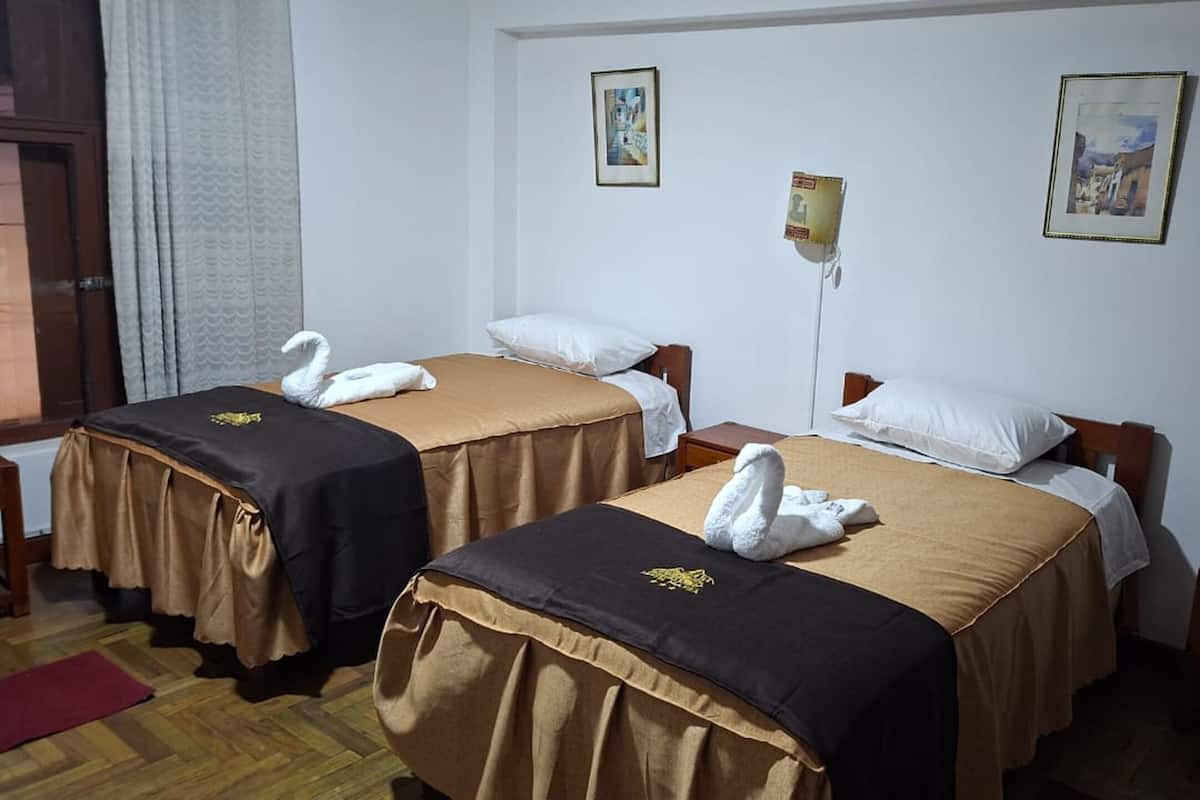 Hotellihuoneessa on kaksi sänkyä, joissa kummassakin on ruskea peitto ja valkoinen tyyny. Seinällä on kaksi kehystettyä kuvaa, huoneessa on puinen yöpöytä ja lattialla punainen matto.