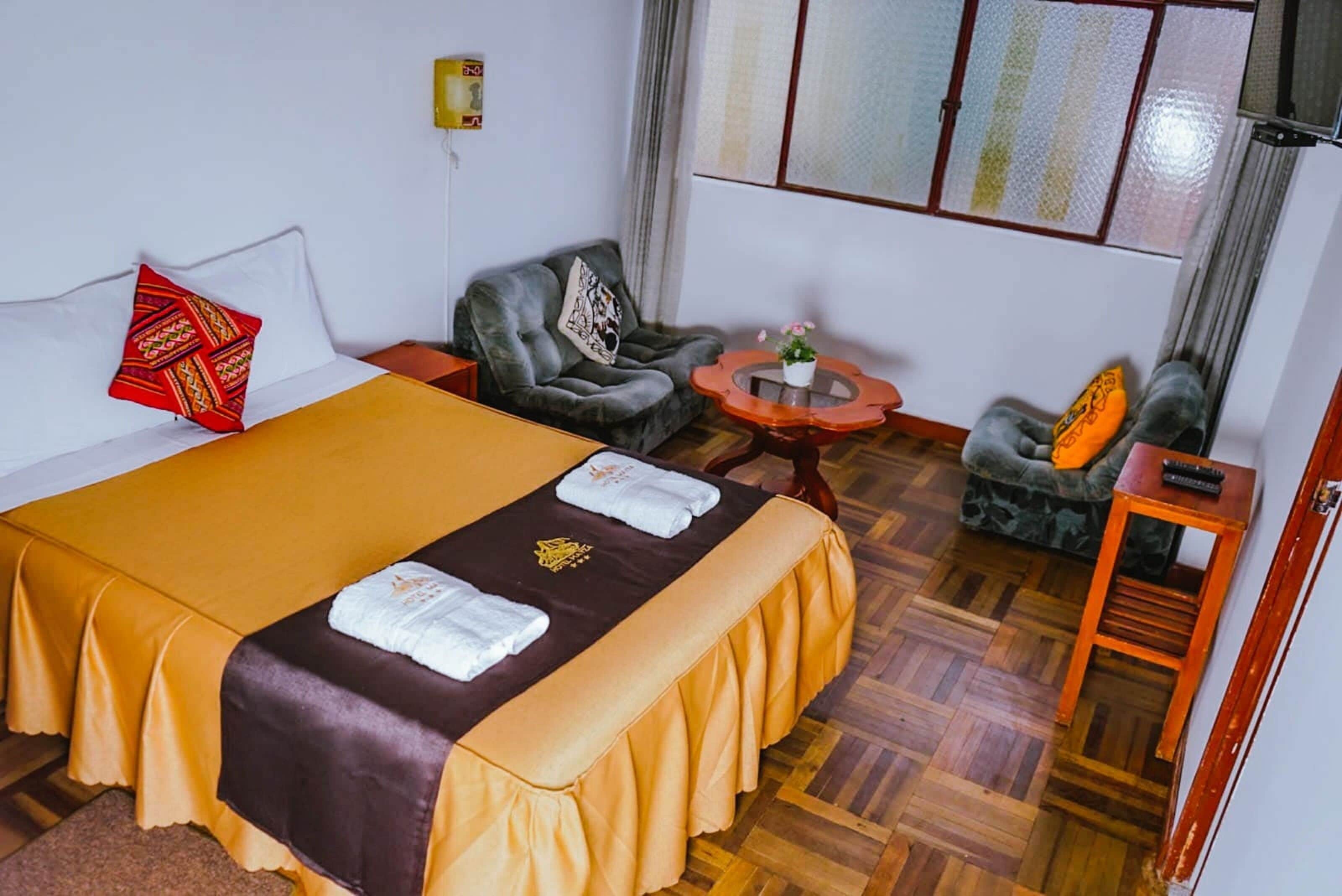 A hotel room with a bed, two armchairs, a small table with a plant, and a window with curtains.