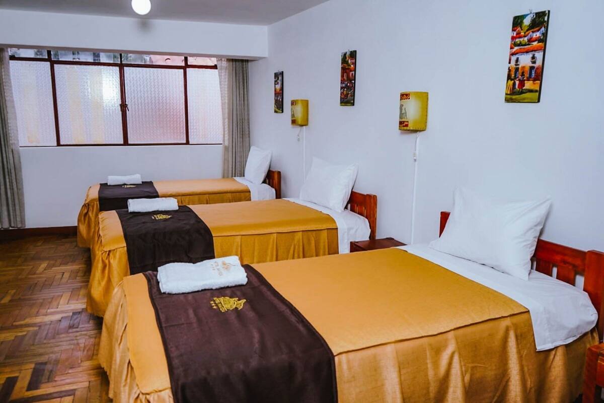 Hotellihuone, jossa on kaksi sänkyä, puulattia ja suuri ikkuna, jossa on verhot.