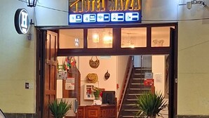 La entrada del Hotel Maya, con un mostrador de recepción, una escalera que conduce al interior y un coche estacionado afuera.