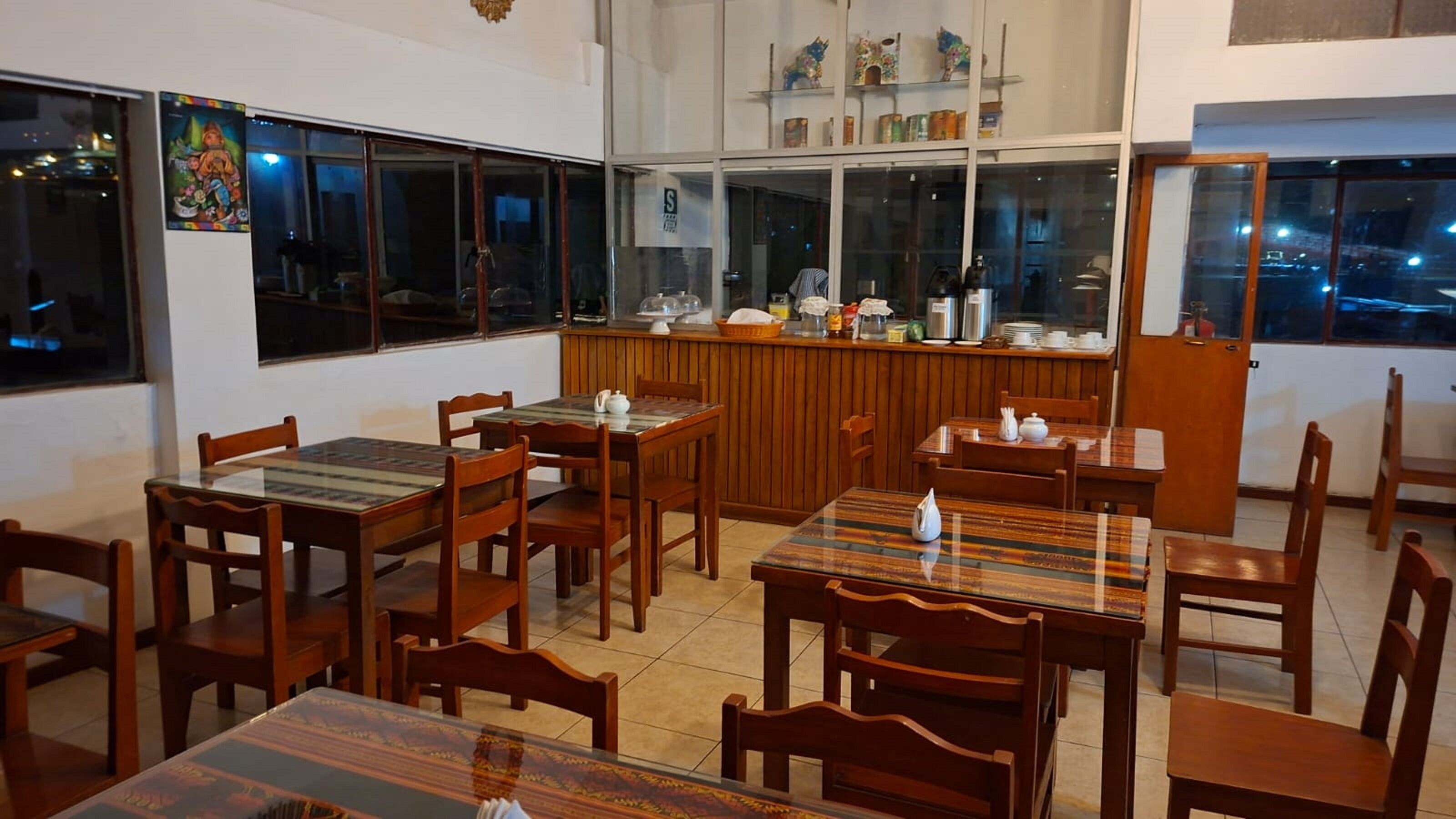 Un ristorante con tavoli e sedie in legno, un bancone con attrezzature da cucina e ampie finestre vista città.