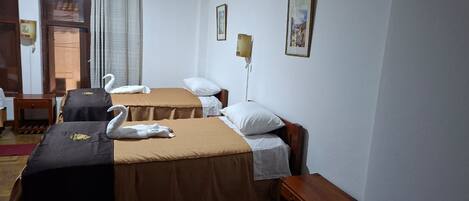 A hotel room with two beds, each with a brown bedspread and white pillows. There are two framed pictures on the wall, a wooden nightstand, and a window with curtains.
