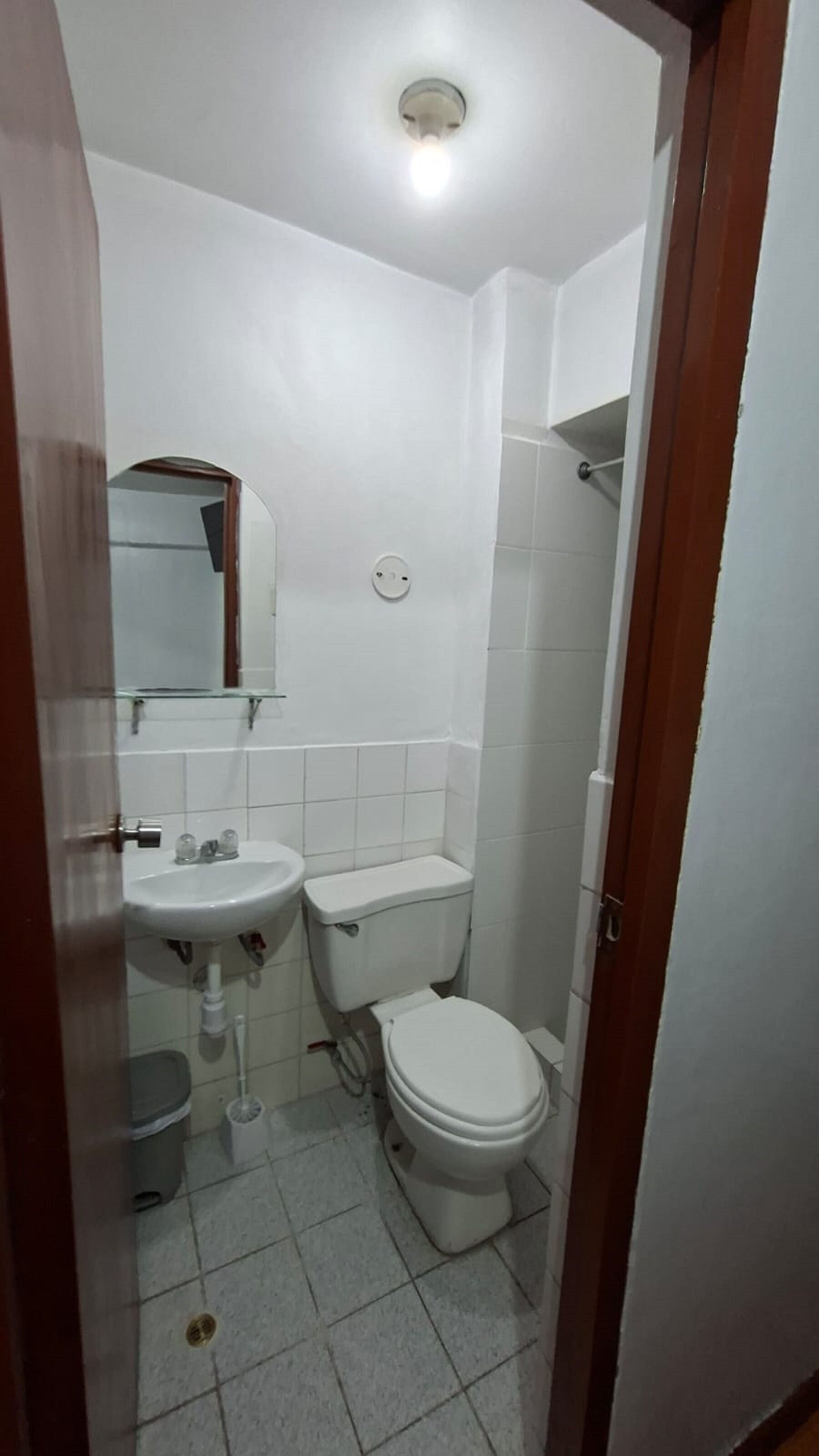 Une petite salle de bain aux dimensions réduites, avec un lavabo, des toilettes et un miroir, le tout de couleur blanche.