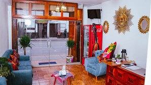 Una sala de estar con un sofá, una mesa de centro y un armario rojo. Se ve una puerta de cristal que da al exterior, y un refrigerador Coca-Cola.