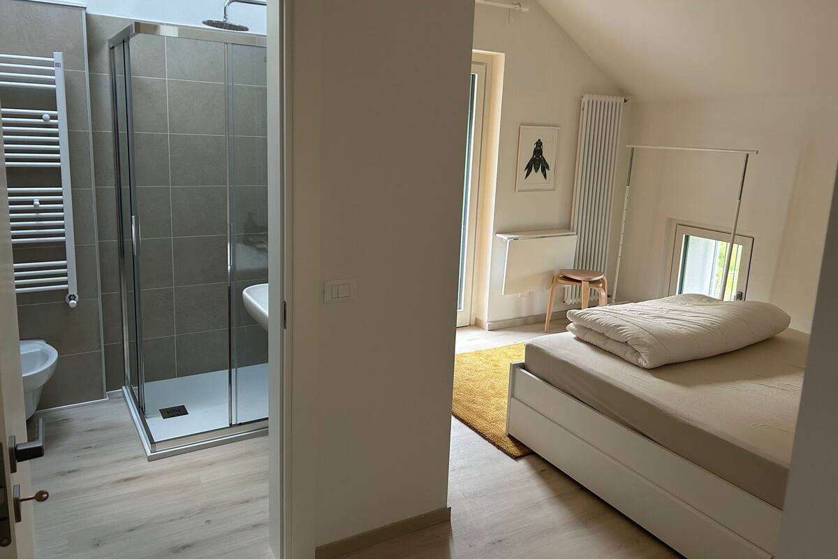 A bedroom with a bed, a window, a radiator, and a bathroom with a shower and toilet.