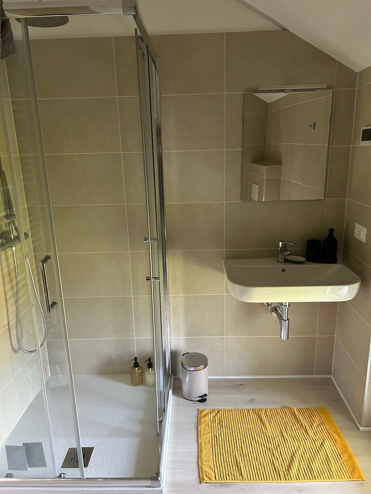 A bathroom with a glass shower enclosure, a sink with a mirror above it, and a yellow mat on the floor.