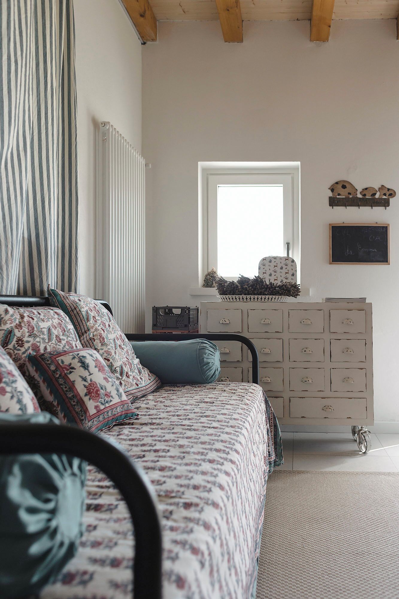 Ein Schlafzimmer mit Bett, Kommode, Heizkörper, Fenster und einer Tafel an der Wand.