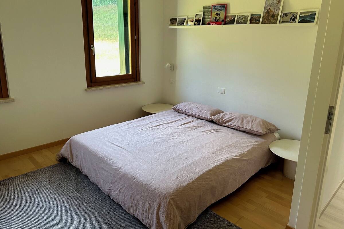 A bedroom with a bed, bedside tables, a window, and a shelf with pictures.