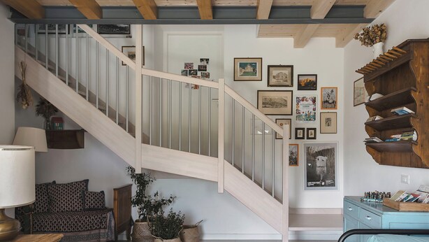 Un escalier avec des marches en bois et une rampe en métal, menant à un palier orné de tableaux encadrés et agrémenté d’une petite bibliothèque.