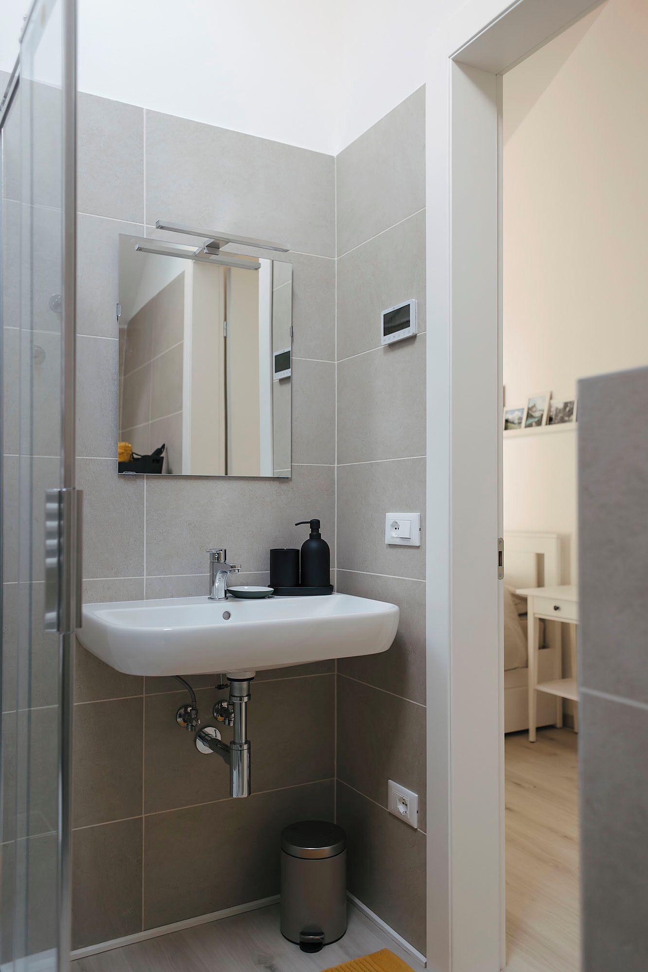 Une salle de bain moderne avec un lavabo blanc, un miroir et une cabine de douche.