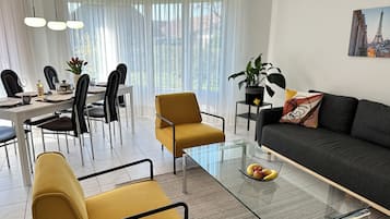 A modern living room with a glass coffee table, a sofa, and a dining area with chairs and a table set for a meal.