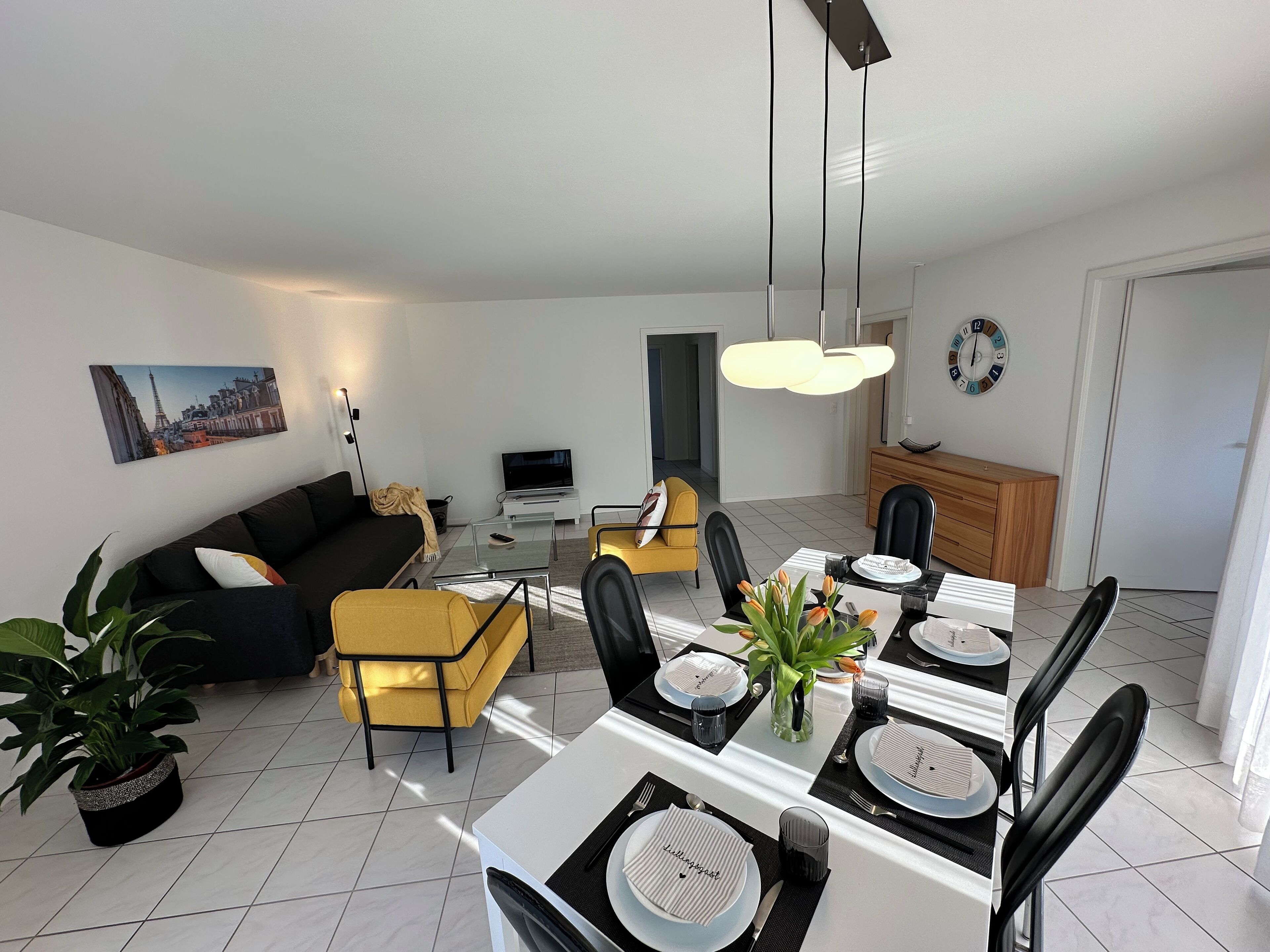 Ett modernt vardagsrum med en soffa, ett matbord för fyra personer och ett köksområde i bakgrunden.