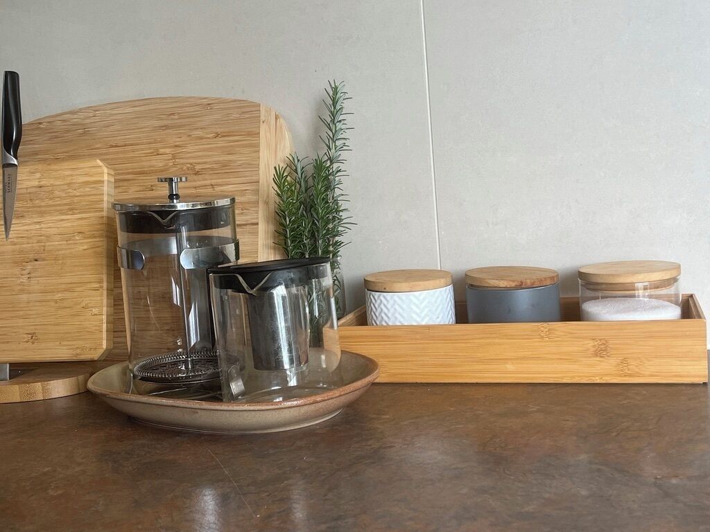 A kitchen counter with a coffee maker, a cutting board, a knife, and several containers.