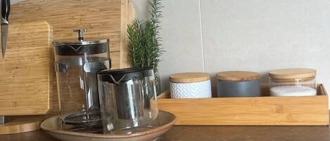 A kitchen counter with a coffee maker, a cutting board, a knife, and several containers.