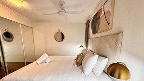 Ein ordentlich bezogenes Bett mit Kissen und einem zusammengerollten Handtuch, eine Nachttischlampe und ein Deckenventilator in einem Hotelzimmer.