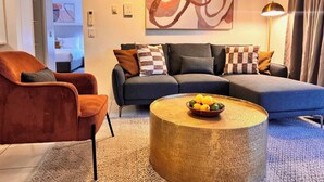 Ein modernes Wohnzimmer mit grauem Sofa, orangem Sessel und rundem Couchtisch mit Obst.