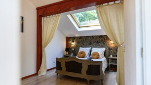 Une chambre avec un puits de lumière, un lit avec deux oreillers, une table de chevet et un mur recouvert d’un papier peint à motifs floraux.