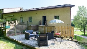 Un bâtiment à l’extérieur jaune, doté d’une terrasse en bois, de mobilier d’extérieur et d’un seul parasol.