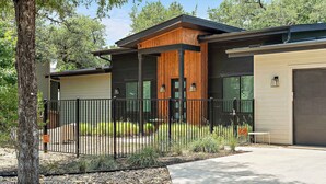 A modern two-story house with a wooden facade, a black metal fence, and a gravel driveway.