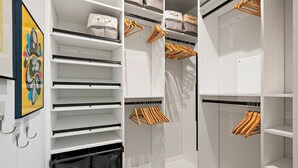 A walk-in closet with multiple shelves, hanging space, and a trash bin.
