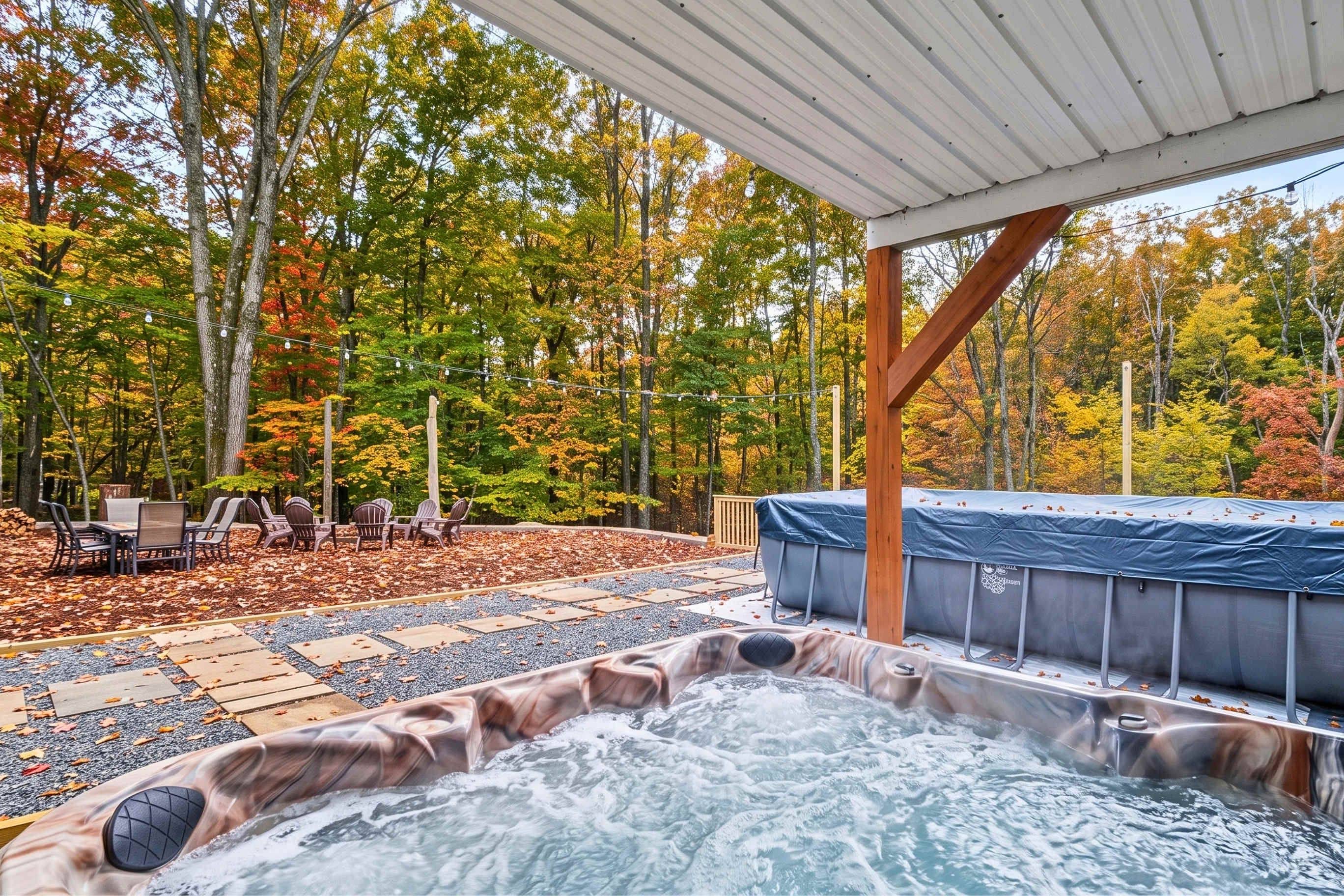 A hot tub with a wooden deck and chairs, surrounded by a forest with autumn foliage.