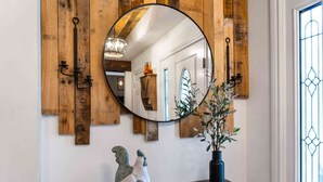 Un espejo redondo sobre un panel de madera, una mesita con un florero de plantas y una escultura decorativa de un pájaro.