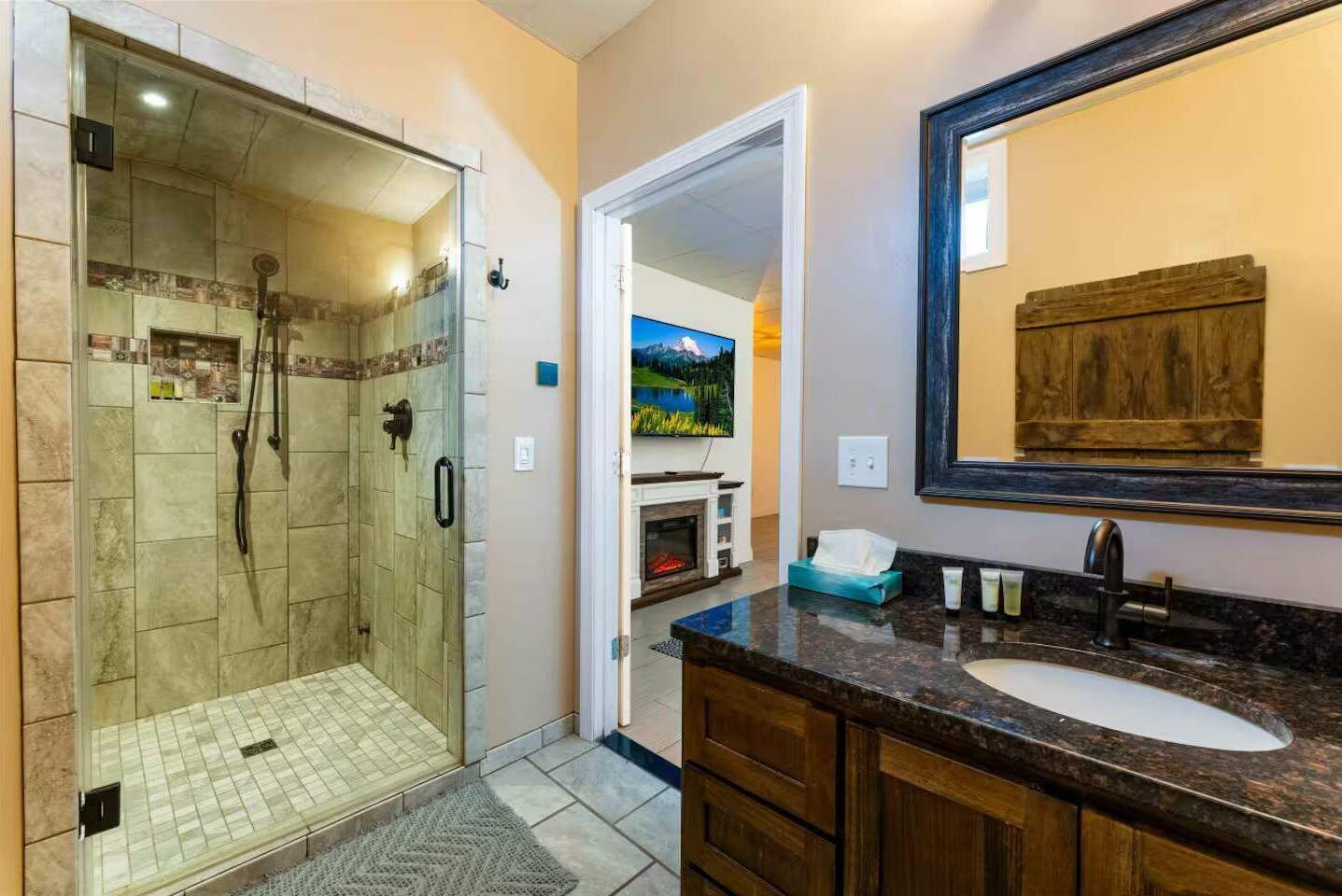A bathroom with a glass-enclosed shower, a sink with a dark countertop, and a wooden vanity.