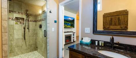 A bathroom with a glass-enclosed shower, a sink with a dark countertop, and a wooden vanity.