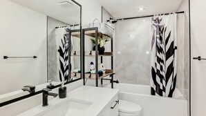 A modern bathroom with a white sink, black faucet, and a large mirror. There is a shower curtain with a leaf pattern, a toilet, and a bathtub. - Cozy 2-bedroom basement suite, fully furnished for comfort and convenience. (Edmonton)
