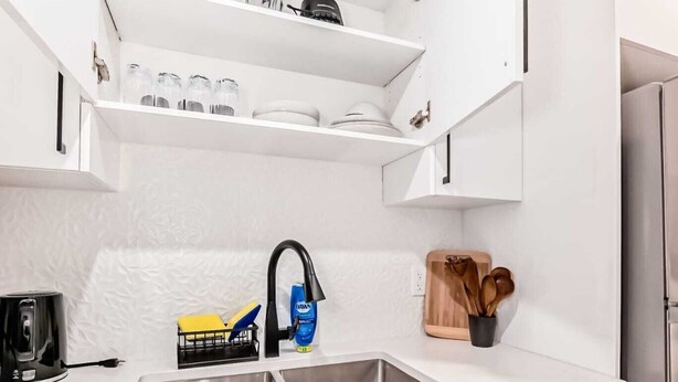 A compact kitchen with white cabinets, a stainless steel sink, and a coffee maker. - Cozy 2-bedroom basement suite, fully furnished for comfort and convenience. (Edmonton)