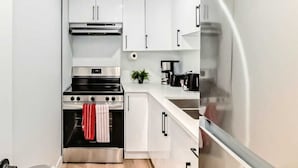 A narrow kitchen with white cabinets, a stainless steel stove, and a refrigerator. - Cozy 2-bedroom basement suite, fully furnished for comfort and convenience. (Edmonton)