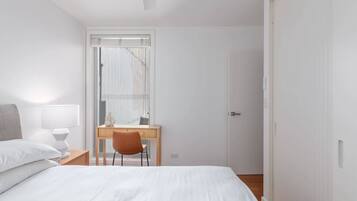 A minimalist hotel room with a bed, a desk, and a chair.