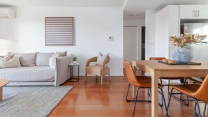 A modern living room with a sofa, a dining table with chairs, a small side table, and a decorative vase.