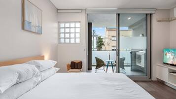 Une chambre d’hôtel avec un grand lit, une chaise, une petite table, un téléviseur et une porte-fenêtre coulissante donnant sur un espace extérieur.