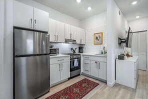 A modern kitchen with white cabinets, stainless steel appliances, and a red patterned rug.