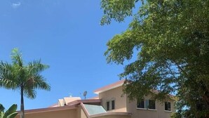 A two-story house with a driveway, parked cars, and a lawn. - CH 1003: Cozy studio with kitchenette, WiFi & Pool, CH 1003: Cozy studio in amazing Manatí with AC, ... (Tierras Nuevas Saliente)