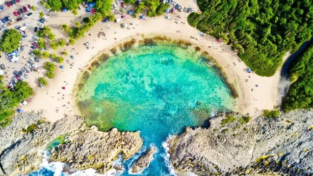 An aerial view of a beach with clear turquoise water, rocky cliffs, and a sandy area with umbrellas and beach chairs. - CH 1003: Cozy studio with kitchenette, WiFi & Pool, CH 1003: Cozy studio in amazing Manatí with AC, ... (Tierras Nuevas Saliente)