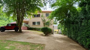 A residential driveway leading to a house with a red vehicle parked nearby. - CH 1003: Cozy studio with kitchenette, WiFi & Pool, CH 1003: Cozy studio in amazing Manatí with AC, ... (Tierras Nuevas Saliente)