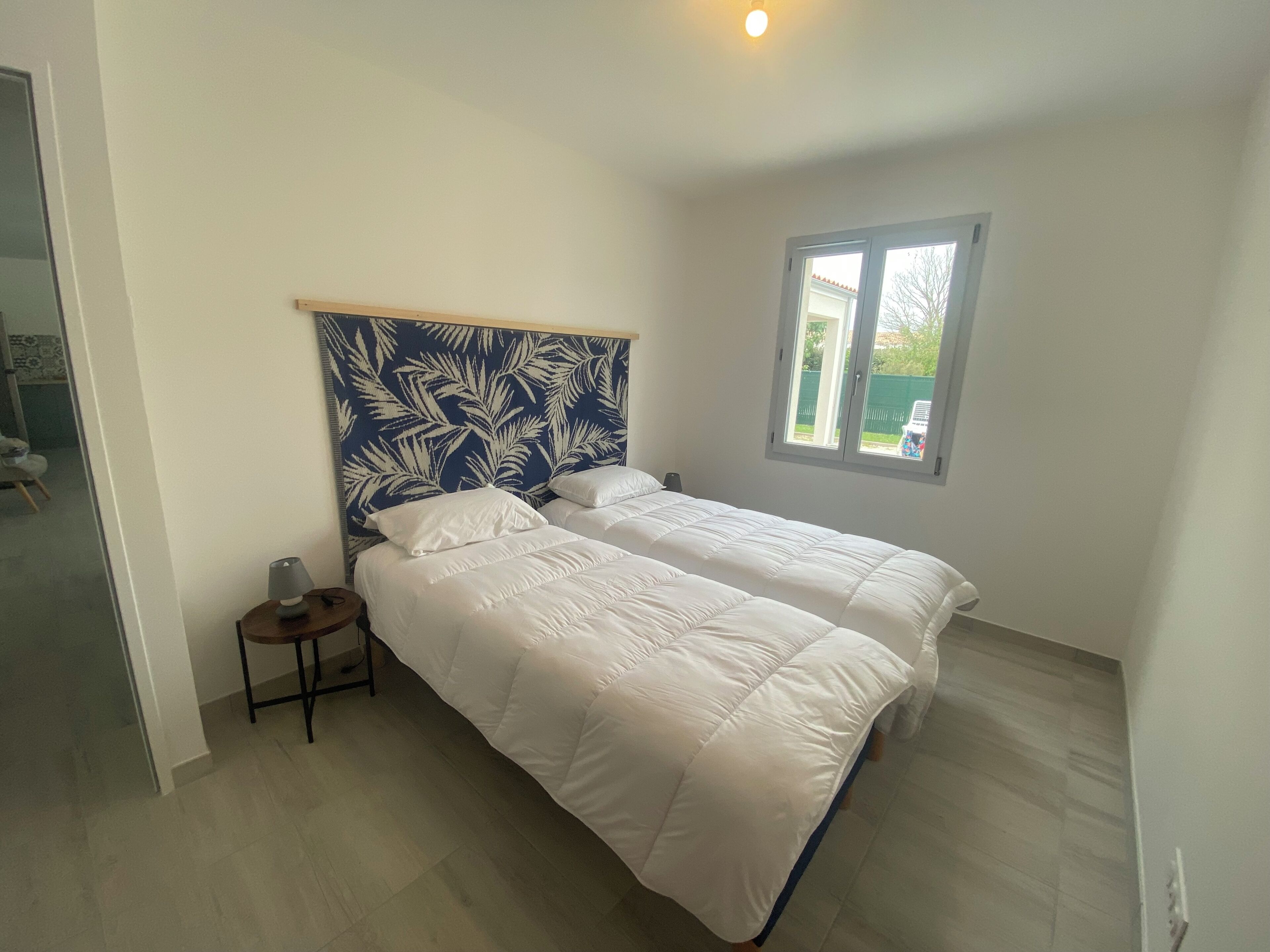 A bedroom with two beds, a nightstand, a window, and a ceiling light.