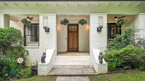 A house with a white brick exterior, a wooden front door, and a covered porch with two ceiling fans. - 10 Mins to Mercedes-Benz Stadium | Dog Friendly (Atlanta)