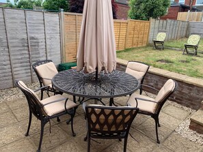 A round metal table with six chairs, surrounded by a wooden fence and a brick wall. - Beautiful home near to Musgrove Park Hospital (Taunton)