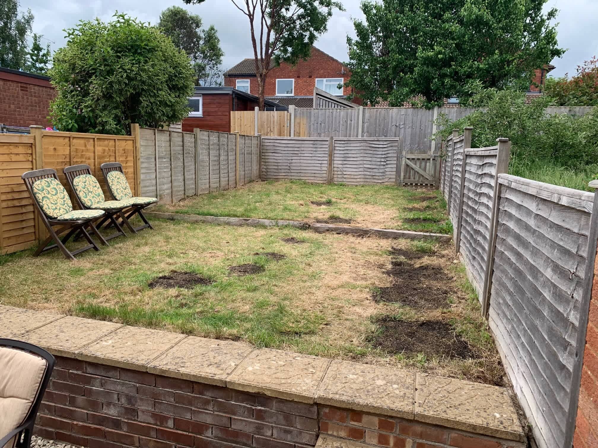 A backyard with a wooden fence, a brick wall, and a grassy area with some patches of dirt.
